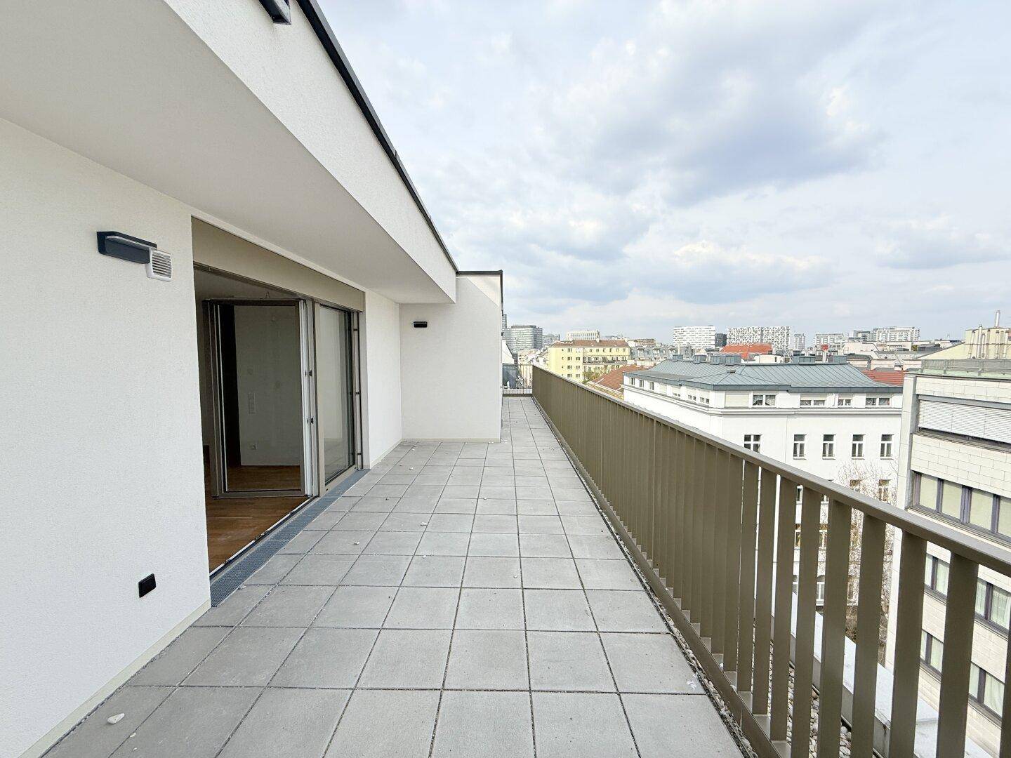 Lange, geflieste Terrasse mit moderner Brüstung und weitem Blick über die Dächer der Stadt.