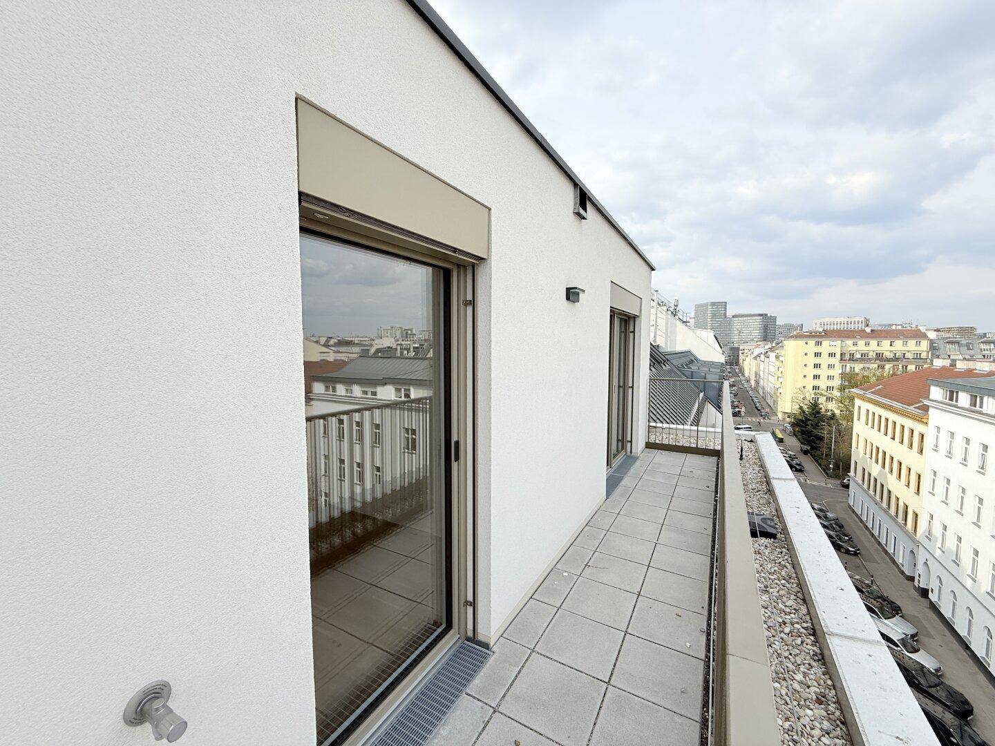 Moderner Balkon mit Fliesenboden und Blick auf die umliegenden Gebäude und die Straße.