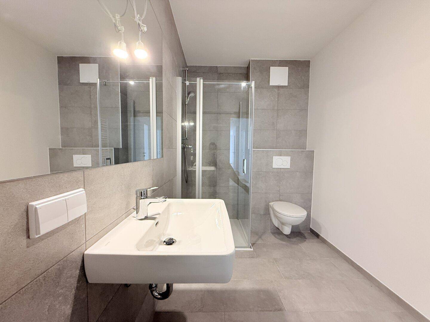Modernes Badezimmer mit Dusche, Waschbecken und Wand-WC, ausgestattet mit grauen Fliesen.