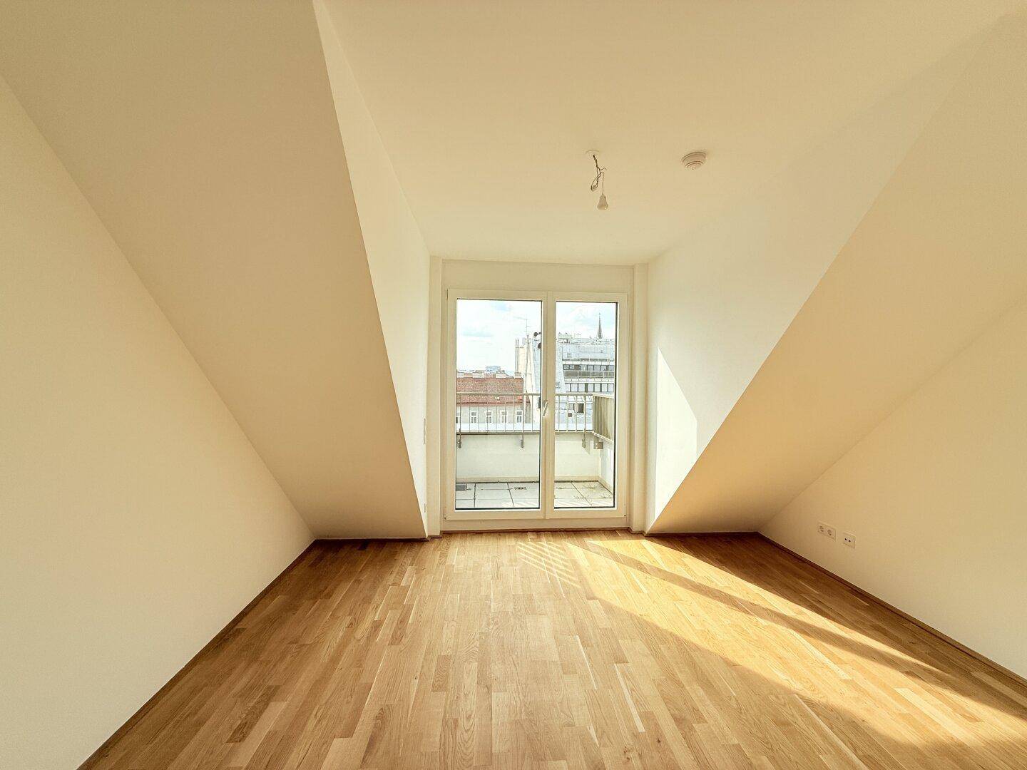 Sonniger Dachgeschossraum mit Parkettboden und Balkonzugang, ideal als Schlafzimmer.