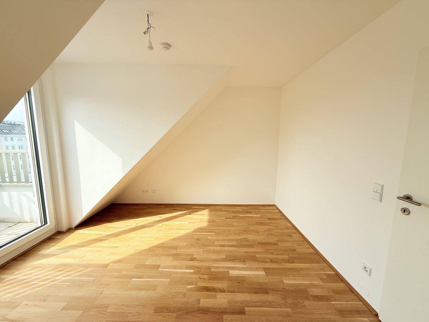 Helles Schlafzimmer mit Parkettboden und direktem Zugang zu einem sonnigen Balkon.