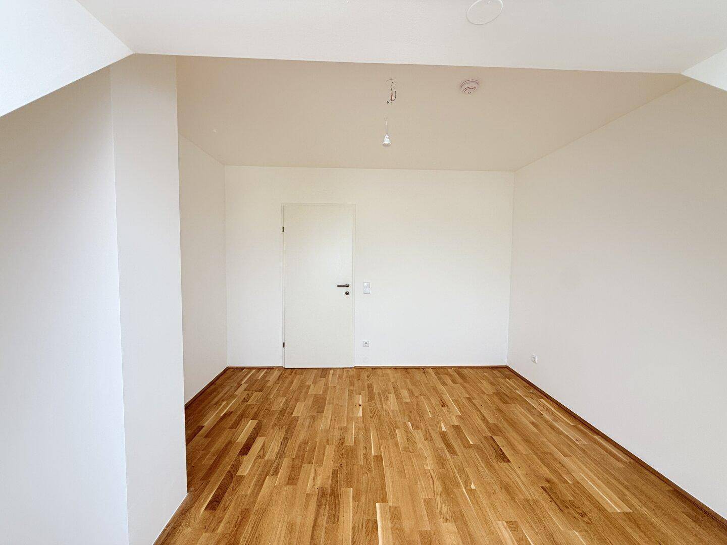 Helles Dachgeschosszimmer mit Parkettboden und weißer Tür, bietet flexible Nutzungsmöglichkeiten.