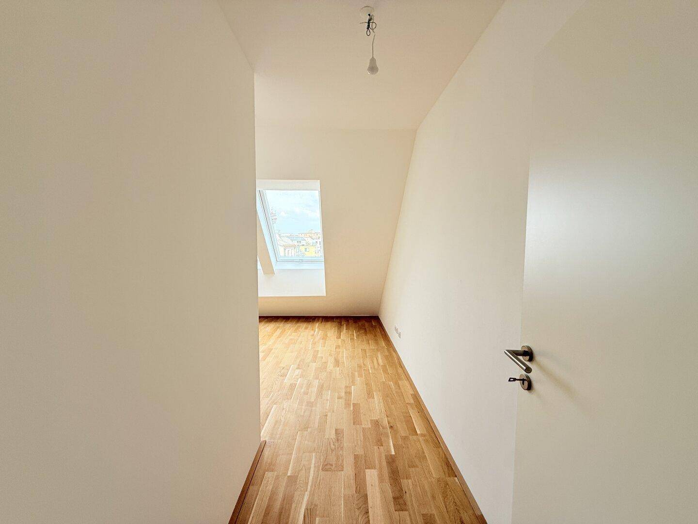 Heller Flur mit Parkettboden, der zu einem lichtdurchfluteten Bereich mit Dachfenster führt.