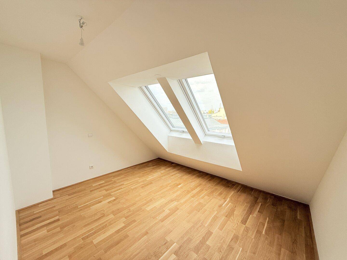 Geräumiges Dachgeschosszimmer mit Parkettboden und zwei großen, schrägen Dachfenstern.