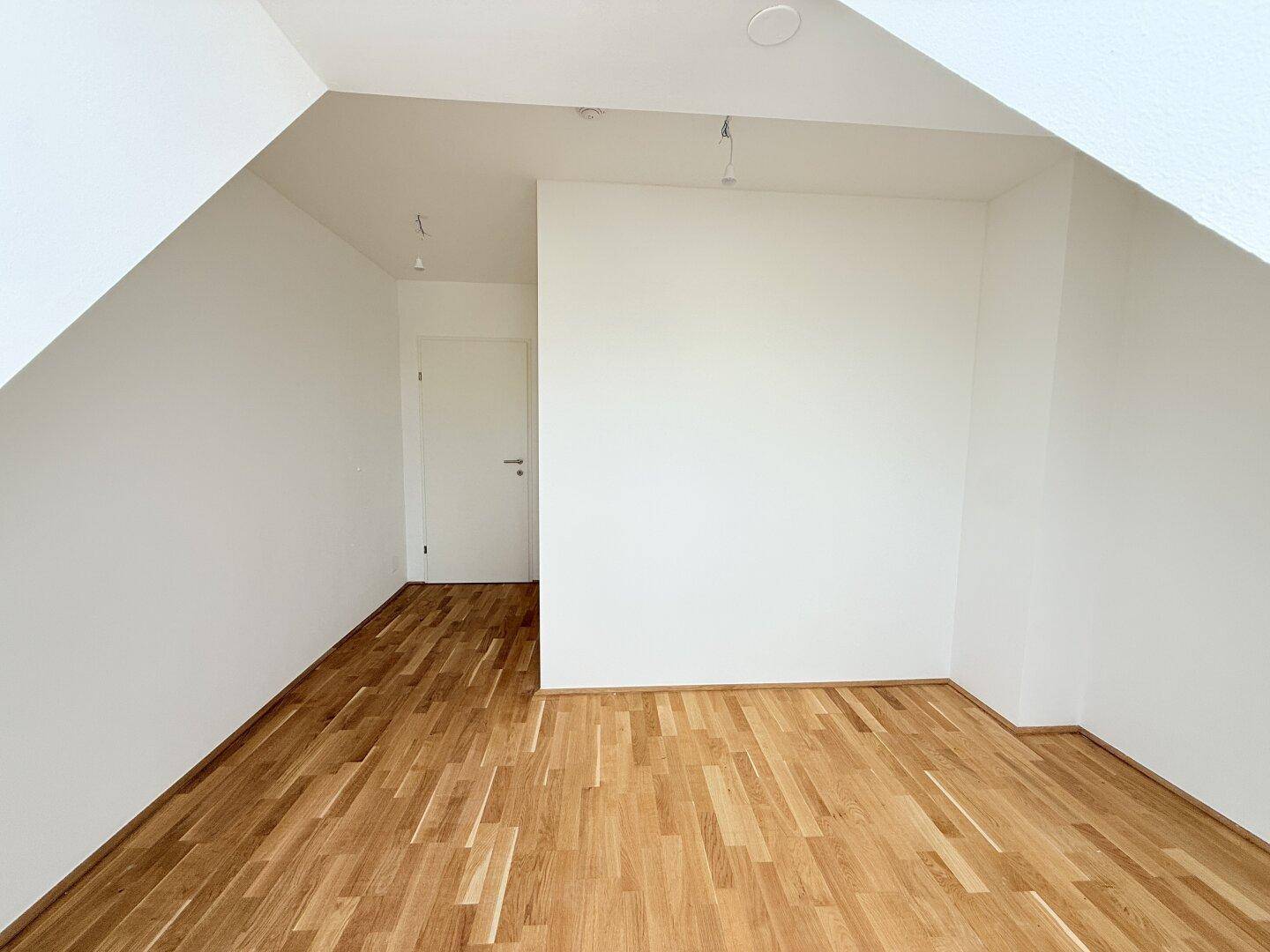 Lichtdurchflutetes Dachgeschosszimmer mit Parkettboden und weißer Tür, bereit zur individuellen Gestaltung.