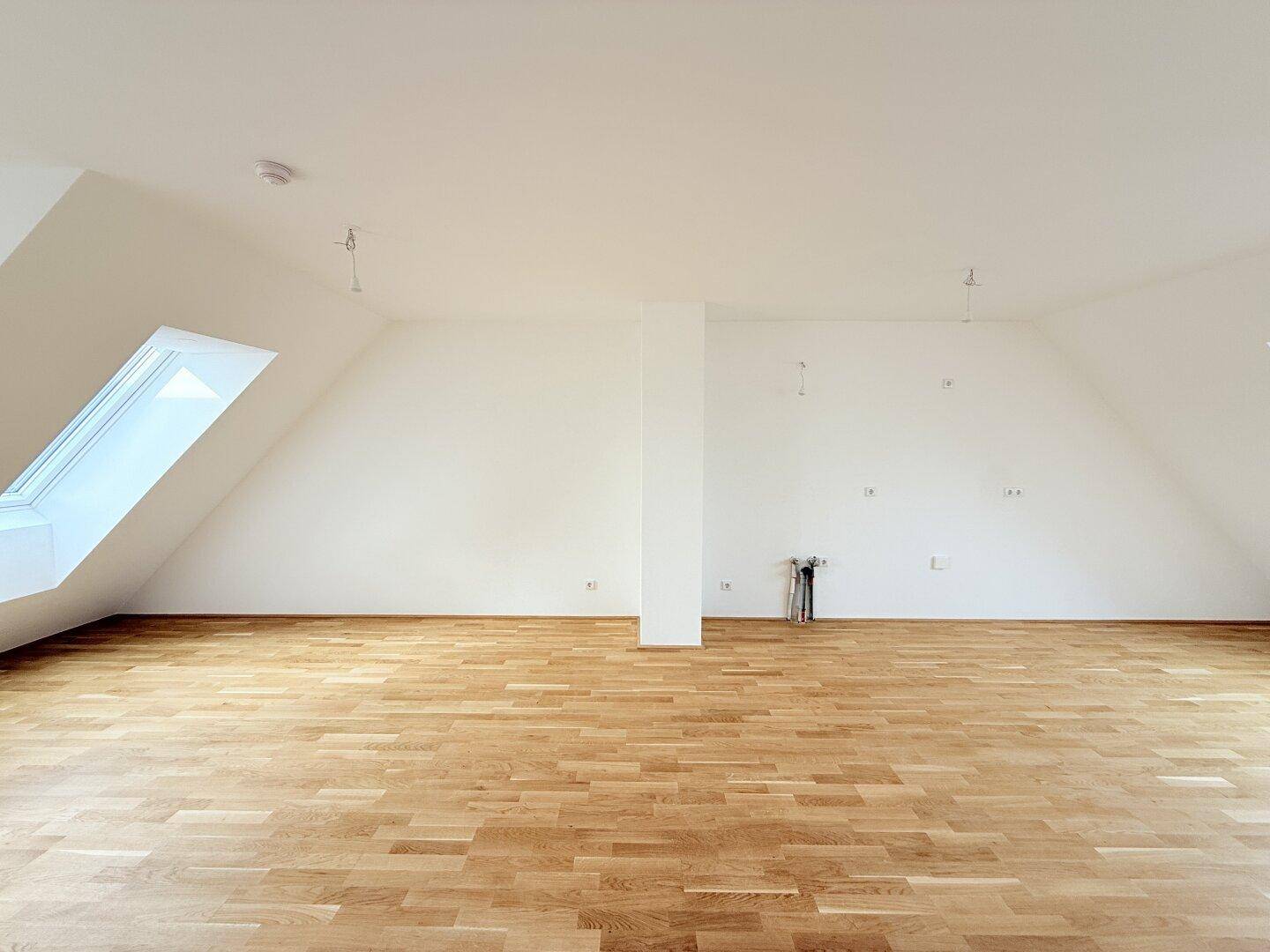 Heller Dachgeschossraum mit Holzboden und schrägen Wänden, bietet vielseitige Nutzungsmöglichkeiten.