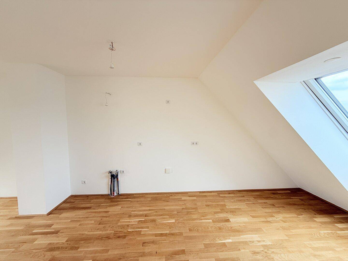 Geräumiger Dachgeschossraum mit Parkettboden und schrägem Dachfenster, ideal für individuelle Gestaltung.