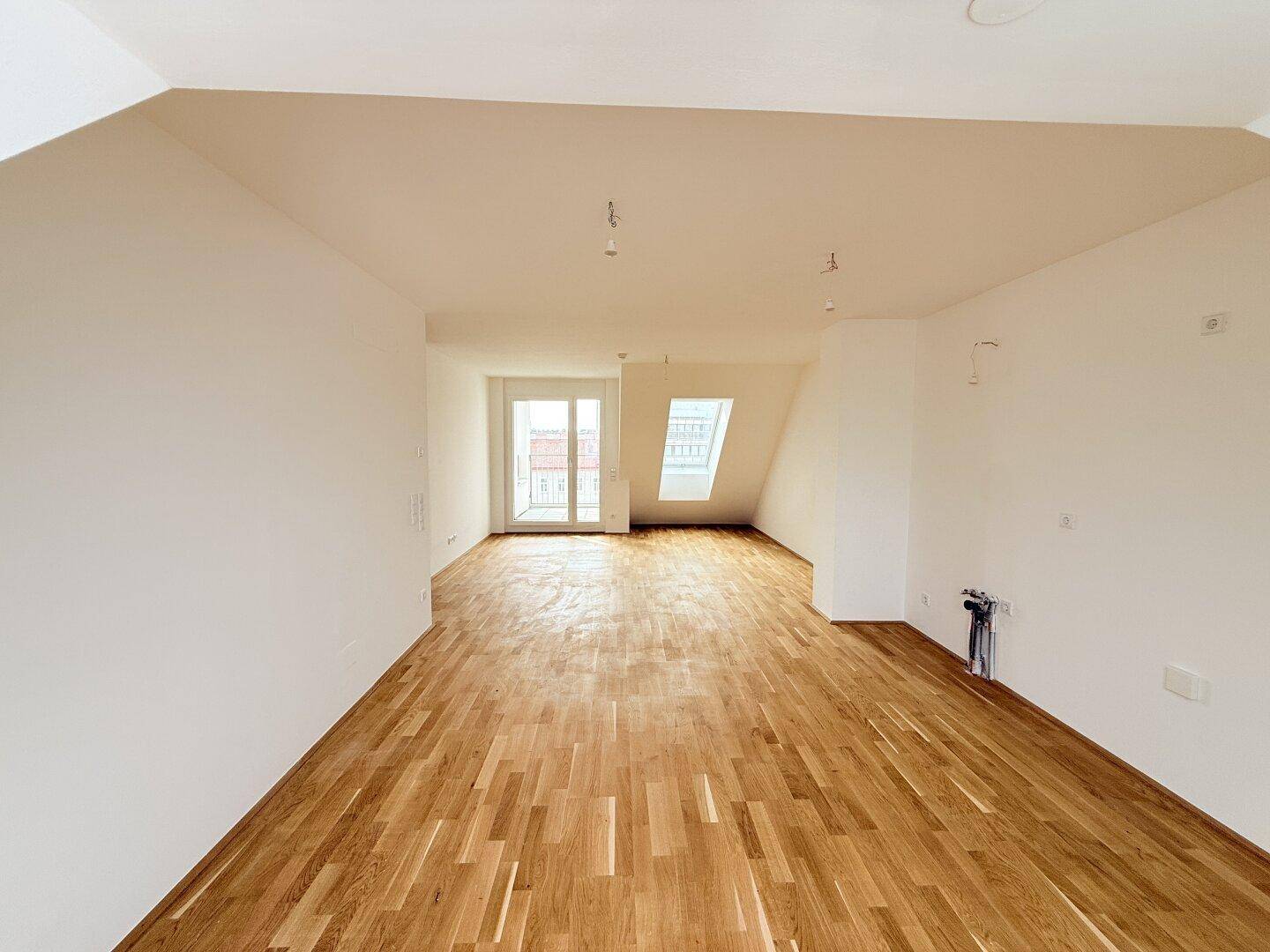 Heller Dachgeschossraum mit Parkettboden, Balkonzugang und zusätzlichem Dachfenster.