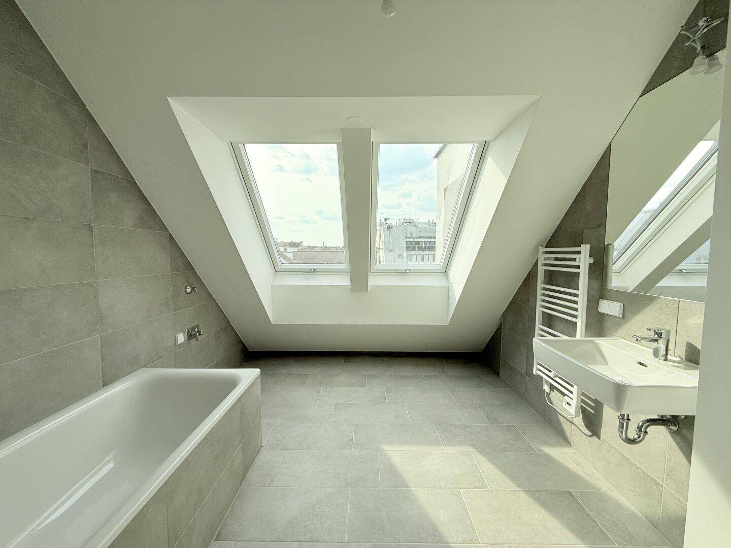 Modernes Badezimmer im Dachgeschoss mit Badewanne, Waschbecken und zwei Dachfenstern.