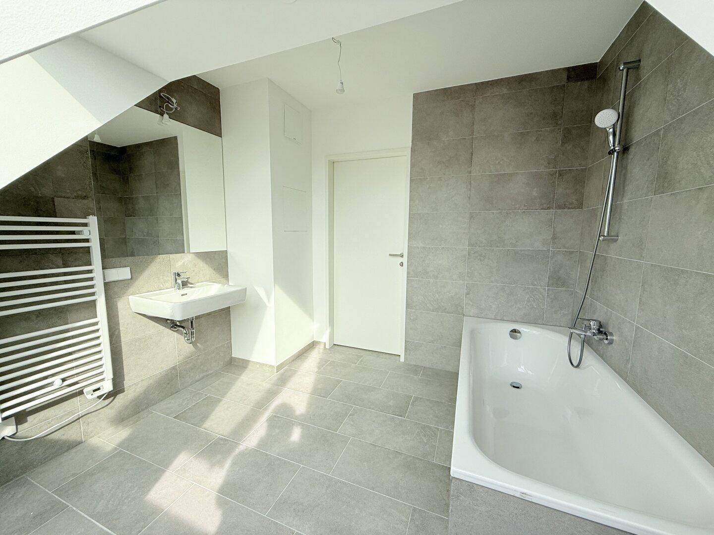 Helles Badezimmer mit Badewanne, Waschbecken und beheiztem Handtuchhalter, modern gefliest.