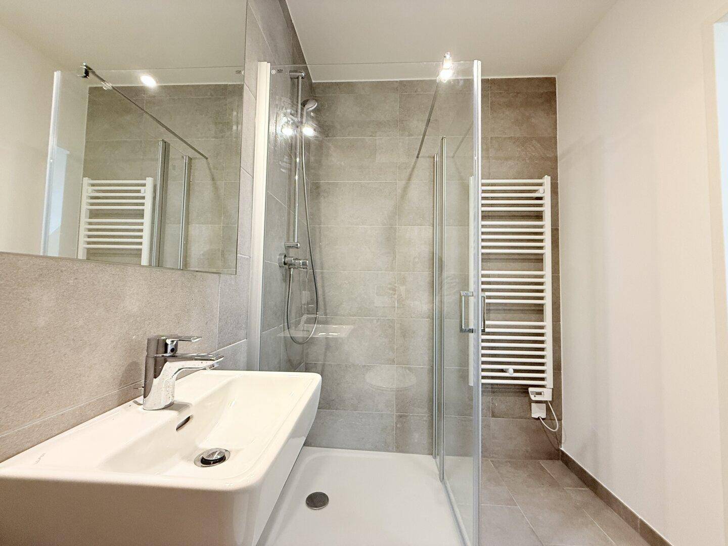 Modernes Badezimmer mit Duschkabine, Waschbecken und beheiztem Handtuchhalter, in hellen Tönen.