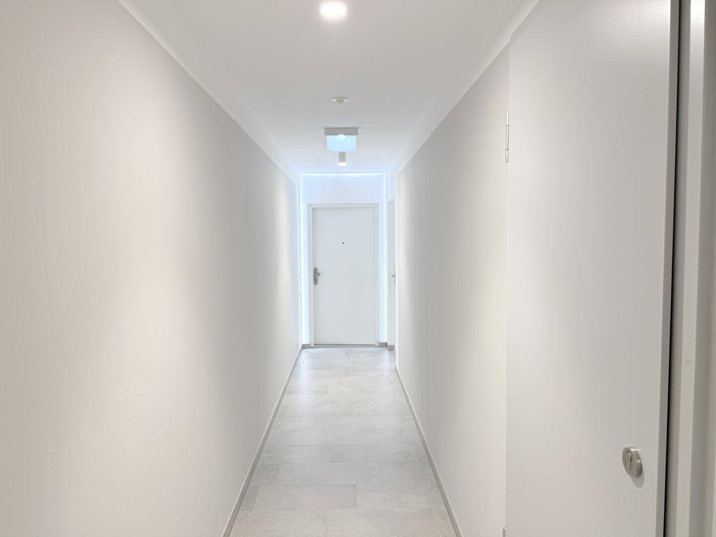 Heller Flur im Gemeinschaftsbereich mit Fliesenboden und weiß gestrichenen Wänden.