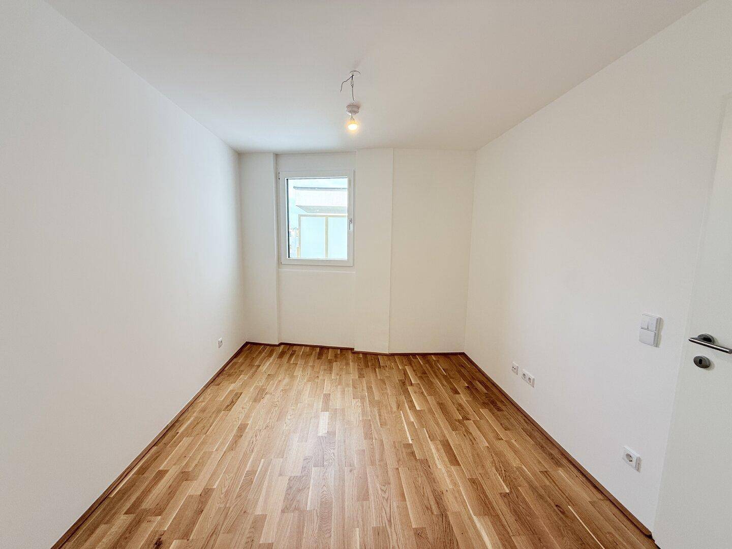 Helles Schlafzimmer mit Parkettboden und einem Fenster, das viel Tageslicht bietet und eine ruhige Umgebung schafft.