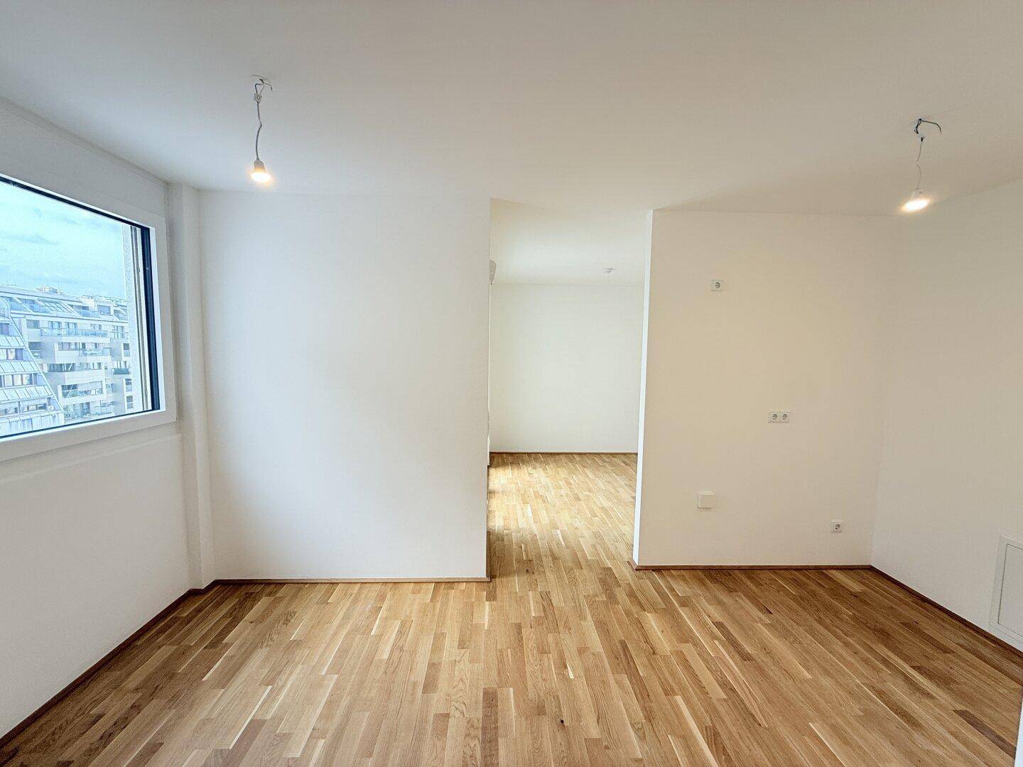 Helles Zimmer mit Parkettboden und einem großen Fenster, das viel Tageslicht hereinlässt und eine angenehme Atmosphäre schafft.