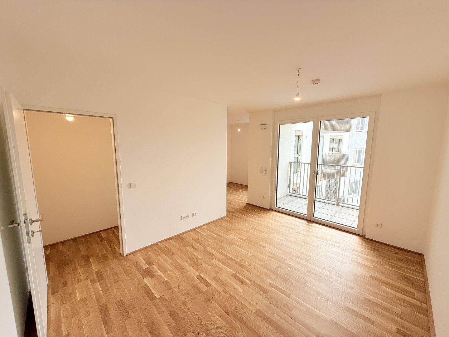 Heller Wohnbereich mit Parkettboden und Zugang zu einem Außenbalkon, der zum Verweilen einlädt.