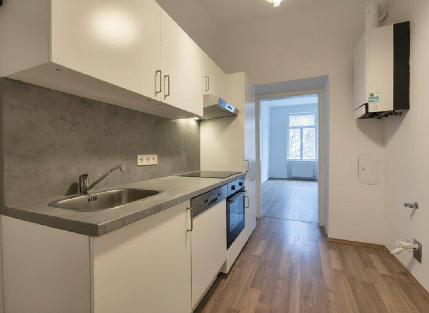 Funktionale Küche mit weißen Schränken, integrierten Geräten und Blick in den angrenzenden Wohnbereich.