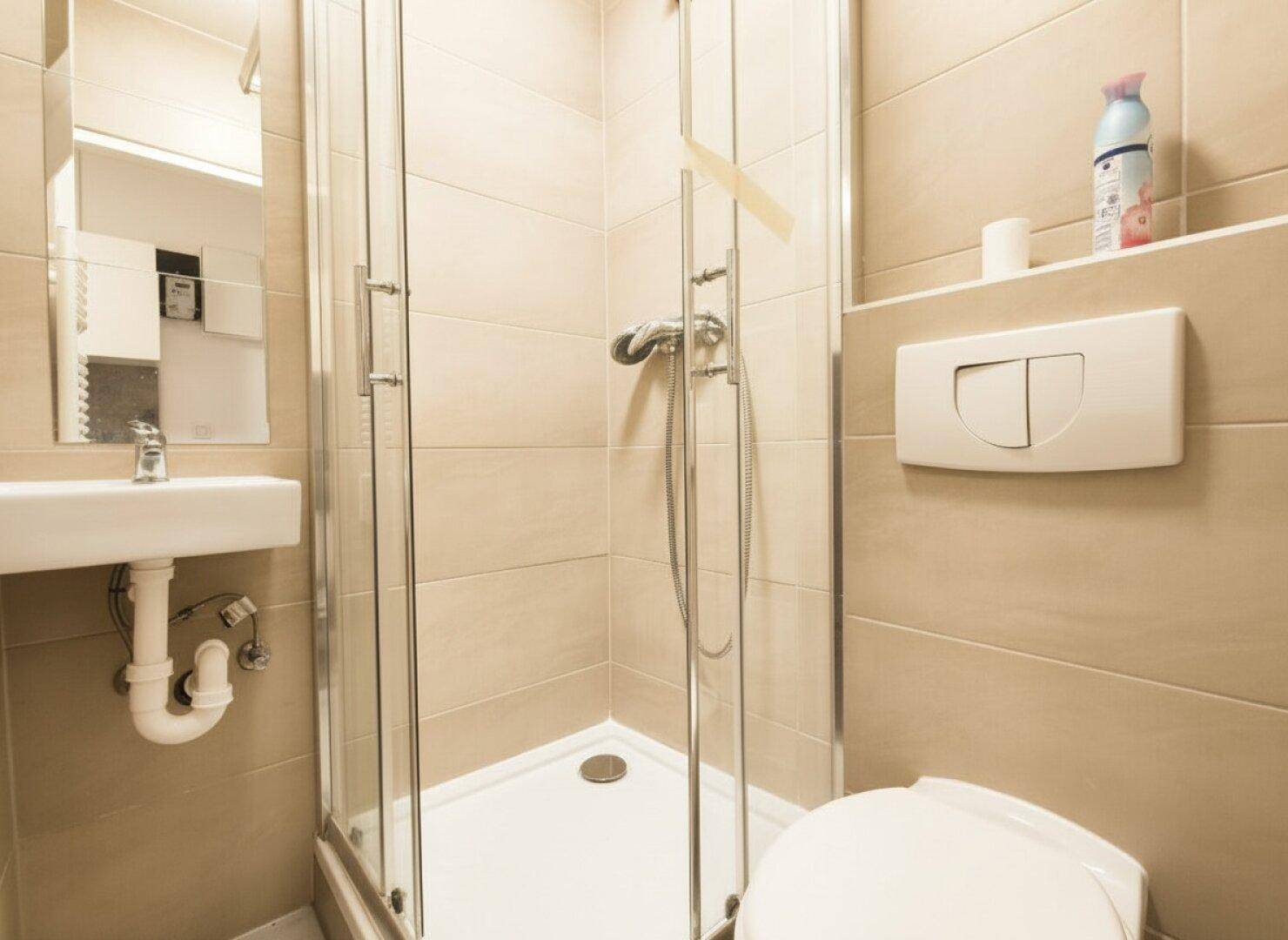 Kleines, funktionales Badezimmer mit Duschkabine, WC und Waschbecken, komplett gefliest in beigen Tönen.