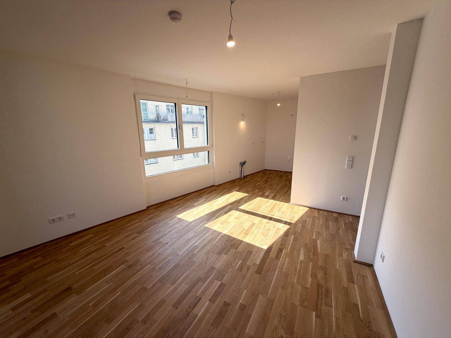 Geräumiger, heller Raum mit Holzparkett und viel Tageslicht durch große Fenster.