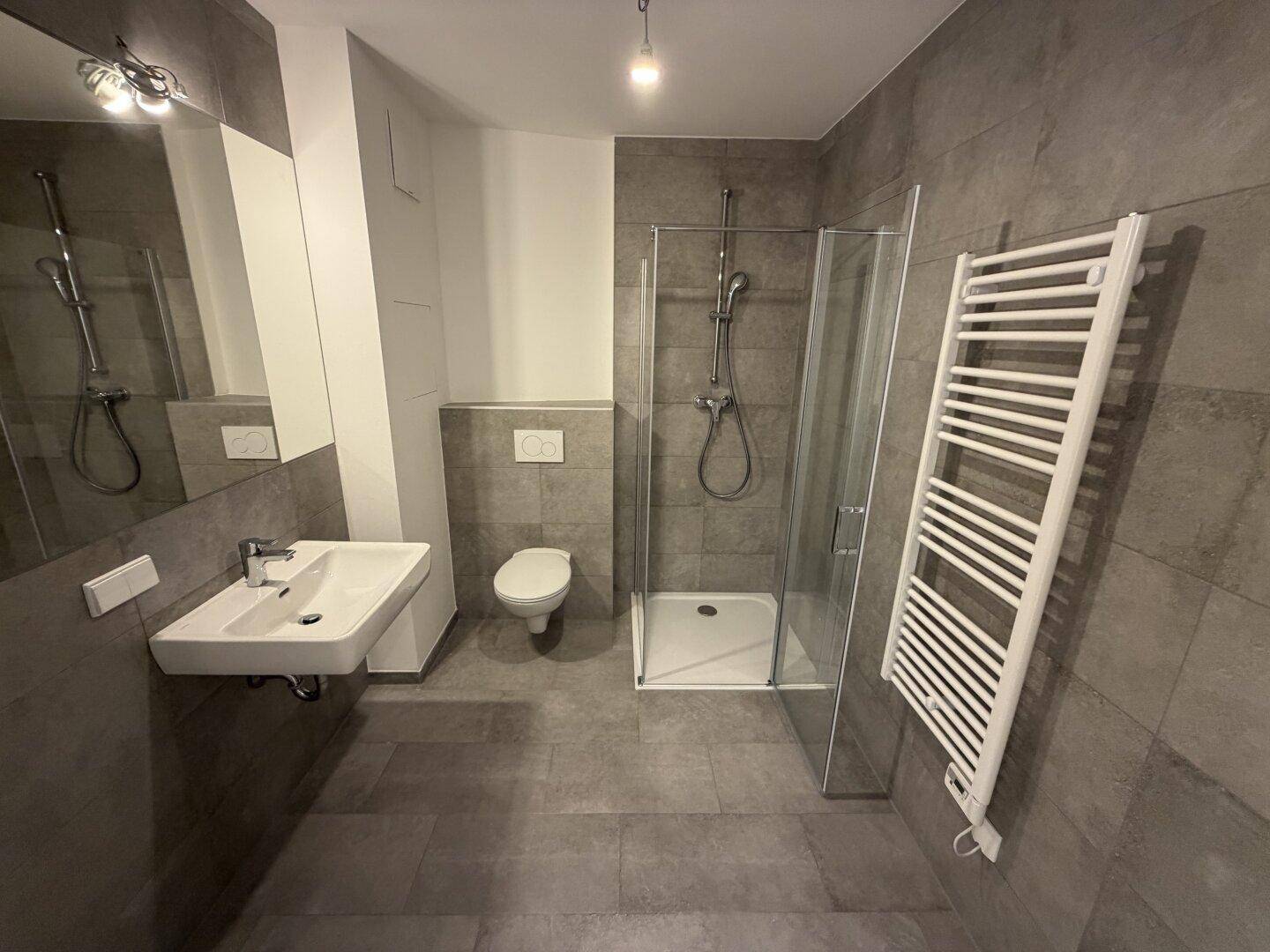 Modernes Badezimmer mit grauen Fliesen, Dusche und beheiztem Handtuchhalter.