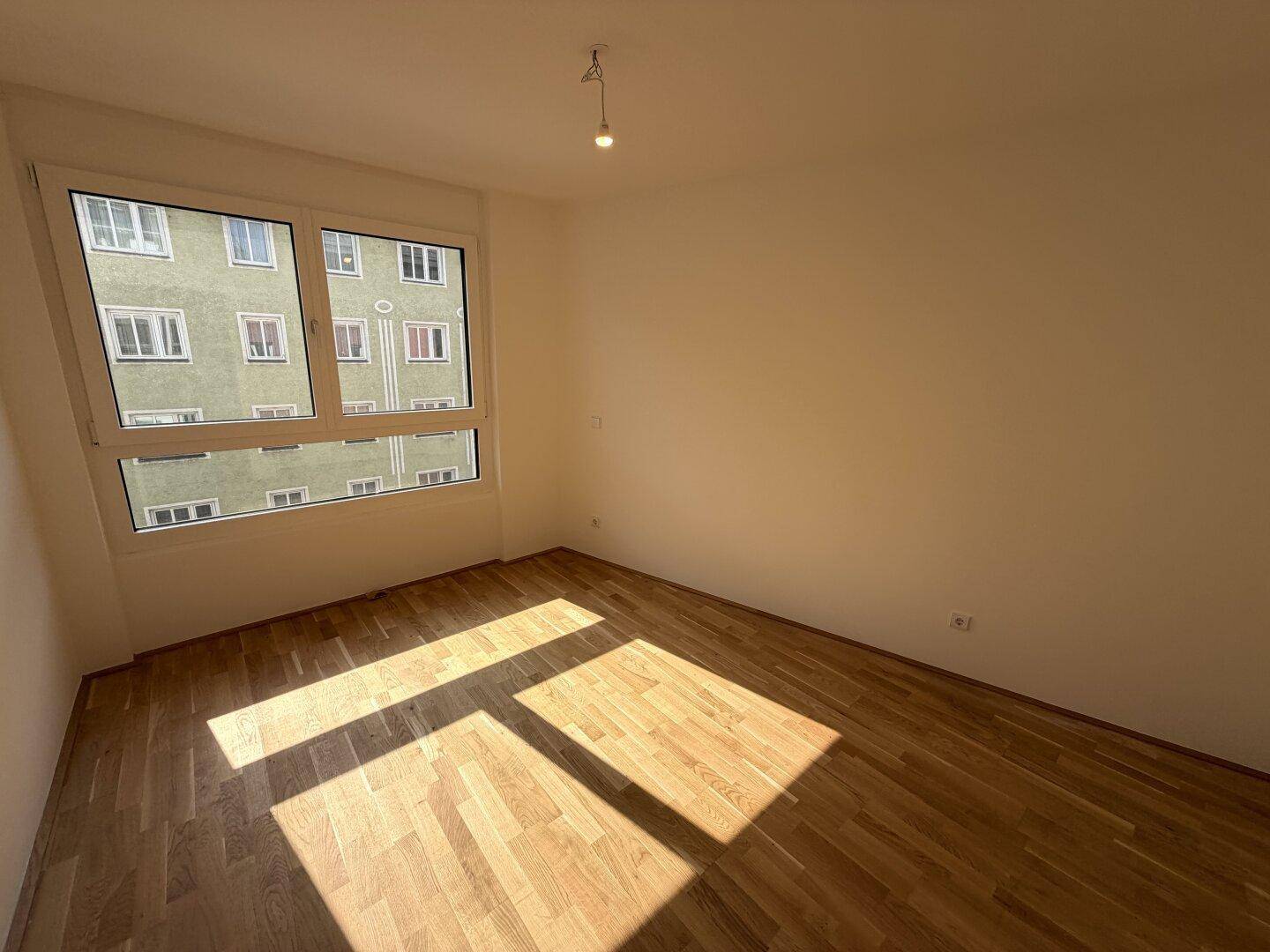 Sonniger Raum mit Parkettboden und großem Fenster, das viel Tageslicht hereinlässt.