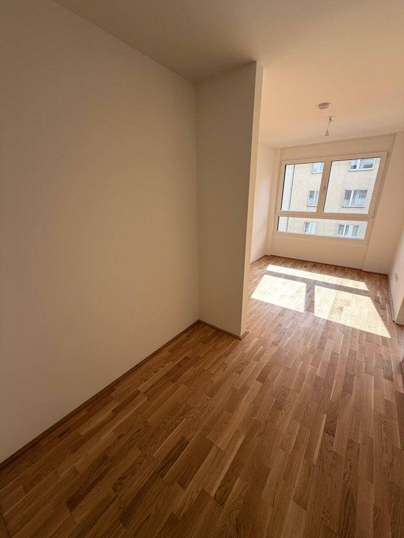 Lichtdurchfluteter Raum mit Holzparkett und Blick auf die umliegenden Gebäude.
