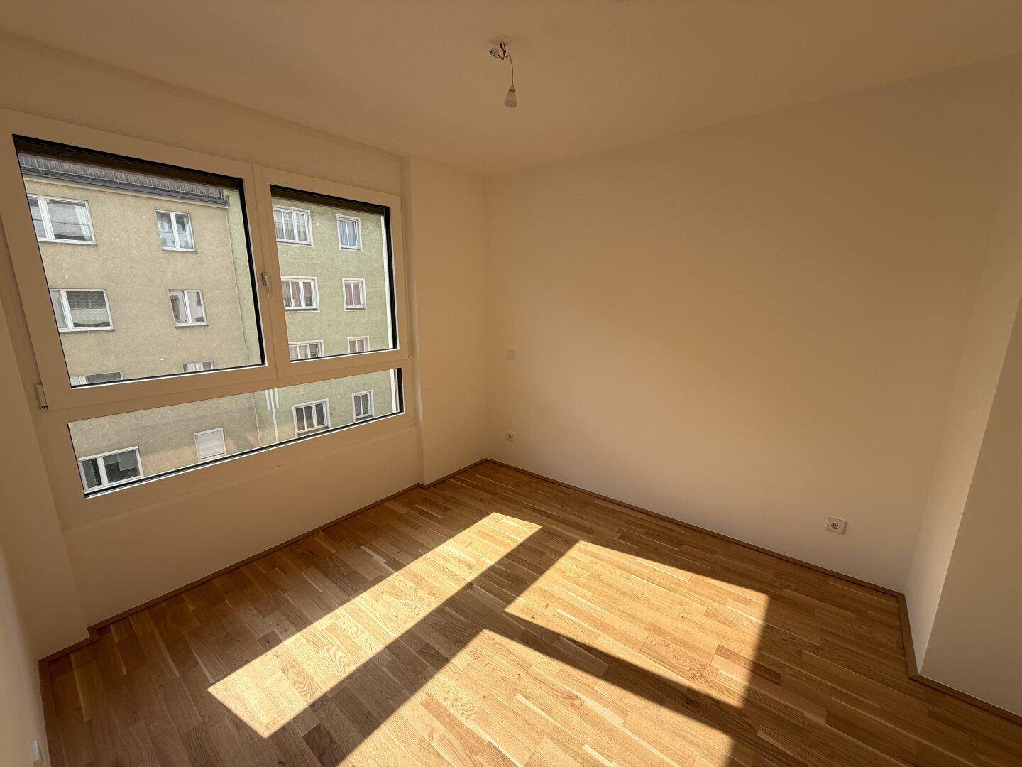 Sonniger Raum mit Parkettboden und großem Fenster, ideal als Schlaf- oder Arbeitszimmer.