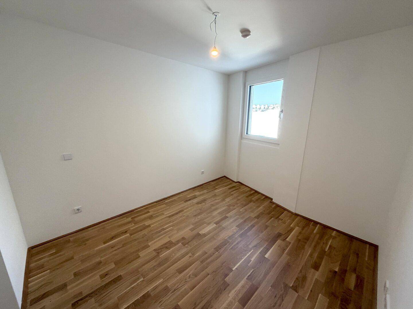 Leerer Raum mit Parkettboden und einem großen Fenster, ideal für individuelle Gestaltung.