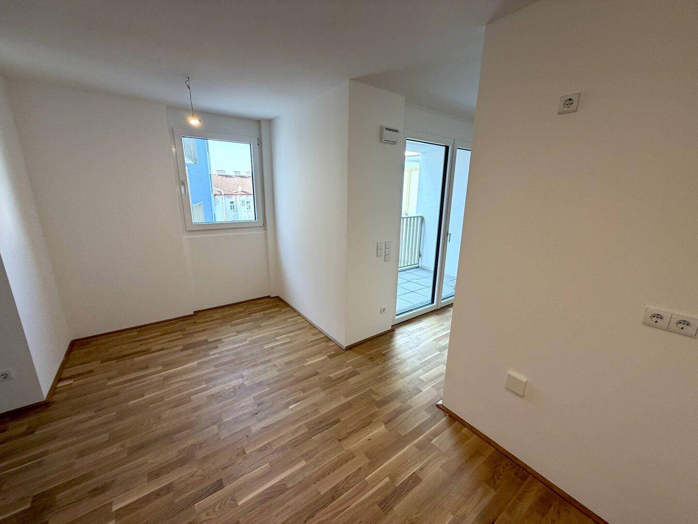 Unmöblierter Raum mit Parkettboden, einem Fenster und Zugang zu einem Außenbereich.