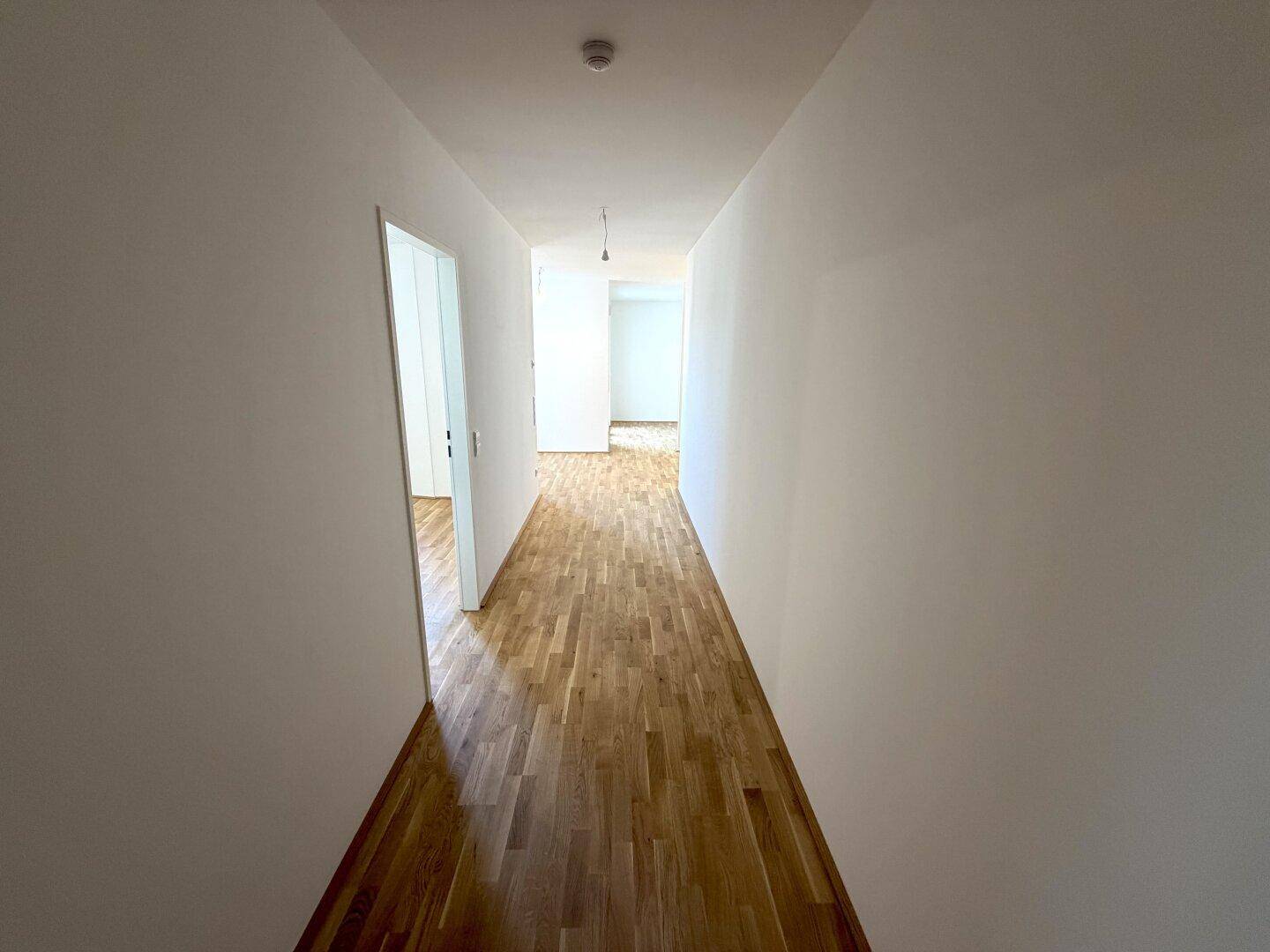 Langer, heller Flur mit Parkettboden, der verschiedene Bereiche der Wohnung verbindet.