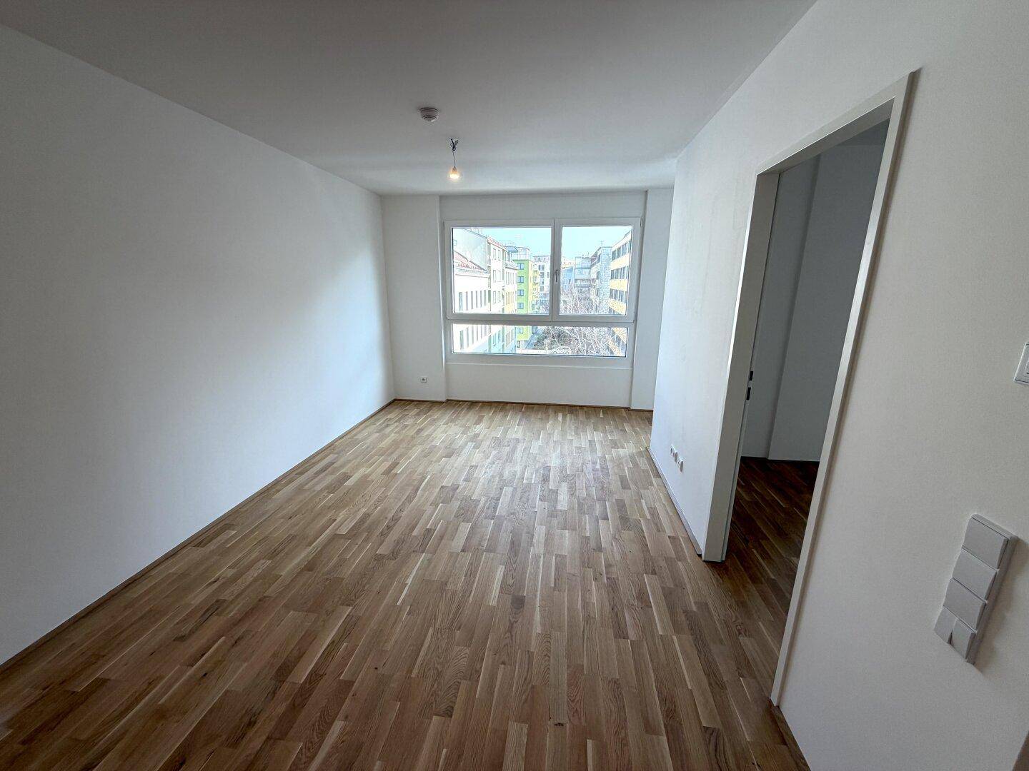 Heller Wohnraum mit Parkettboden, weißen Wänden und großem Fenster zur Straße.