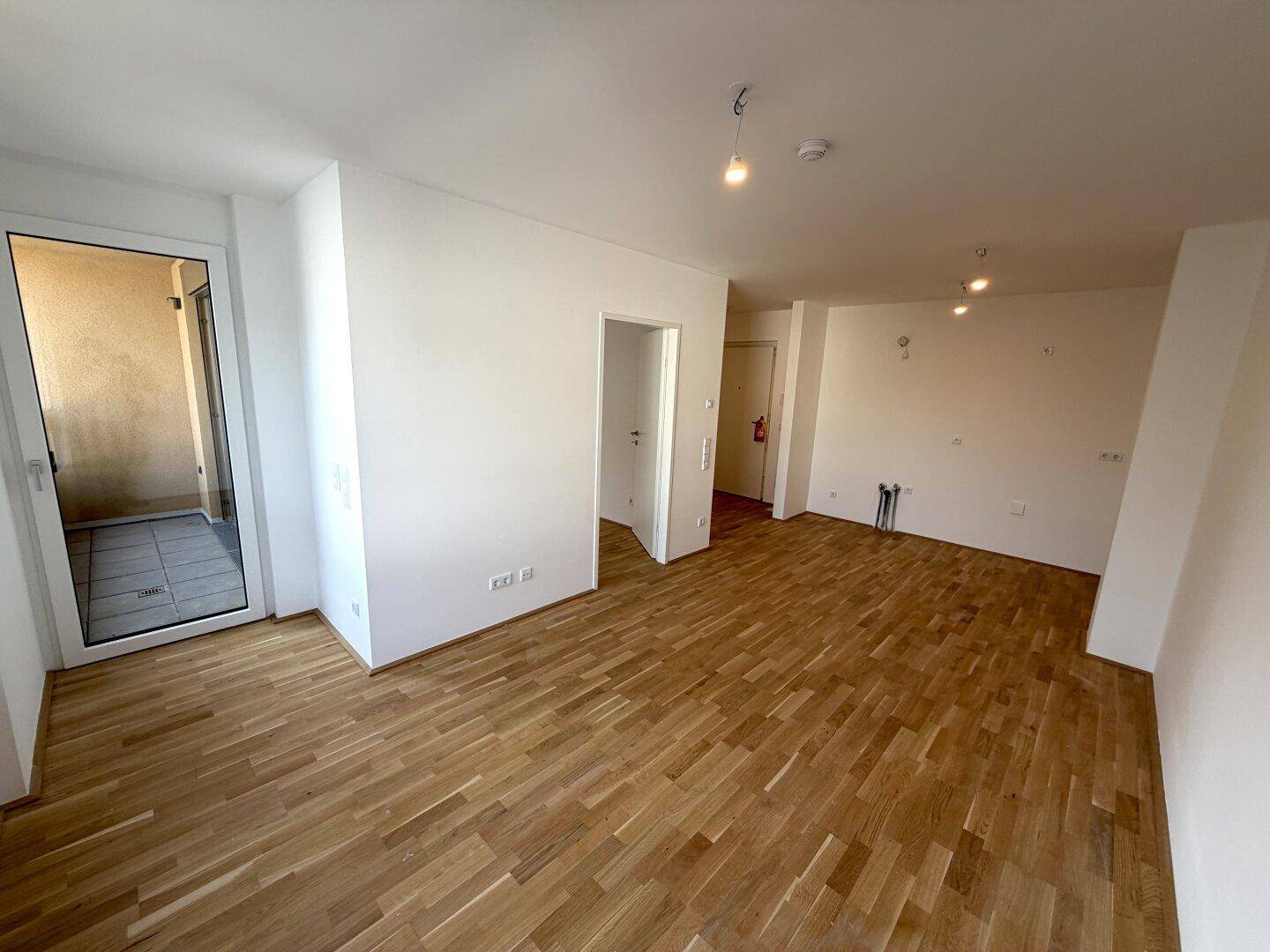Geräumiger offener Wohnbereich mit Parkettboden und Zugang zu einem Außenbereich.