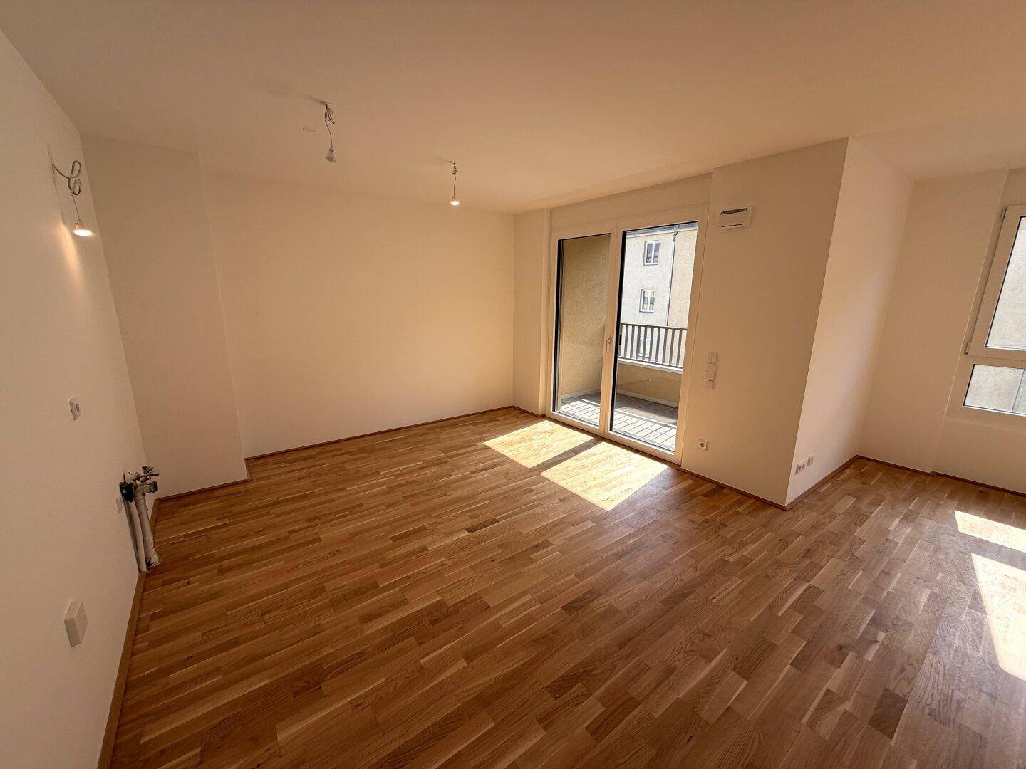 Geräumiger Wohnbereich mit hellem Parkettboden und viel Tageslicht durch die Balkontür.
