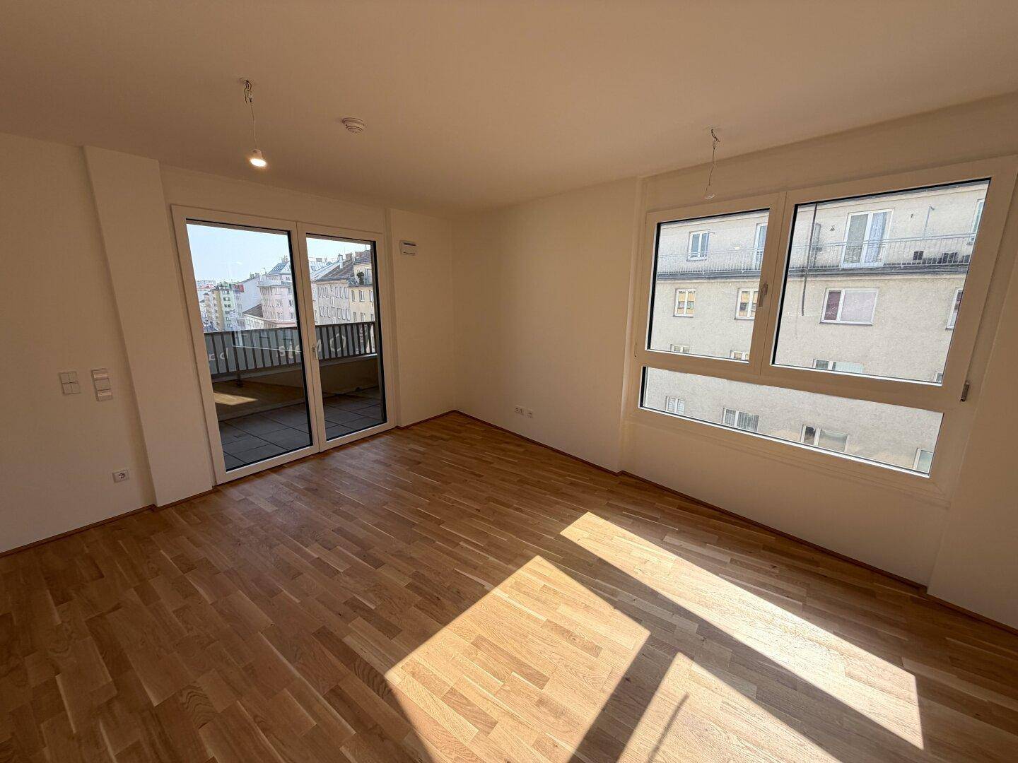 Heller Wohnraum mit Echtholzparkett, großen Fenstern und Zugang zu einem Balkon.