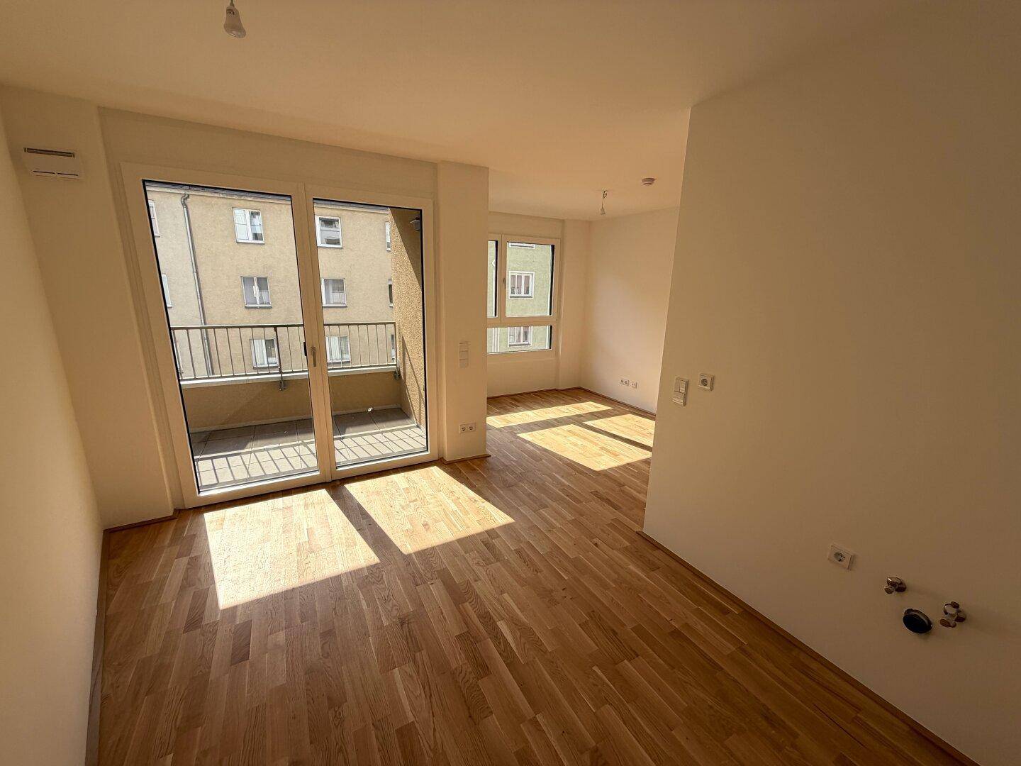 Geräumiger, lichtdurchfluteter Raum mit Parkettboden und Zugang zum Balkon, ideal für offenes Wohnen.