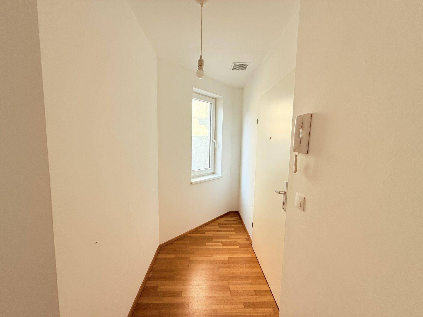 Heller Flur mit Parkettboden und Fenster, ausgestattet mit einer Gegensprechanlage.