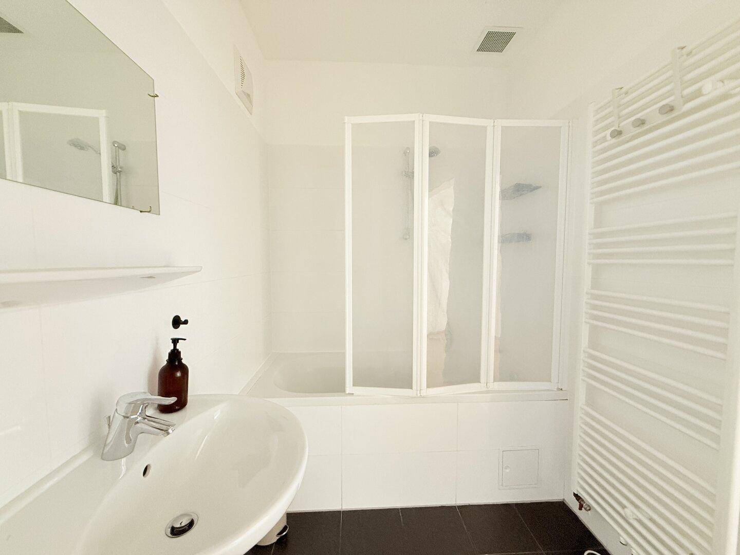 Helles Badezimmer mit Badewanne, Duschwand und beheiztem Handtuchhalter, in modernem Design.