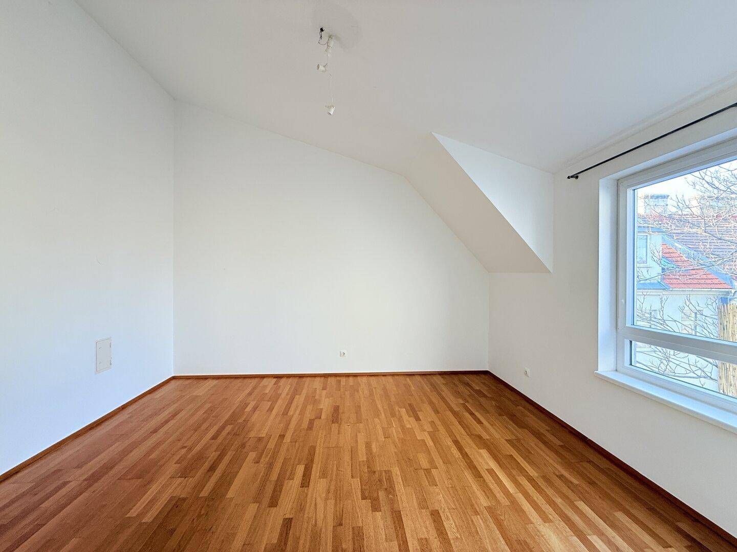 Helles Schlafzimmer mit Parkettboden und Dachschräge, bietet eine ruhige Wohnatmosphäre.