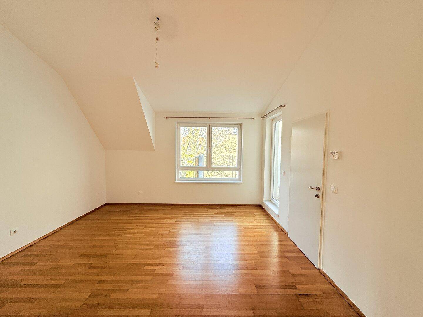 Helles Zimmer mit Parkettboden und schrägen Wänden, bietet vielseitige Nutzungsmöglichkeiten.