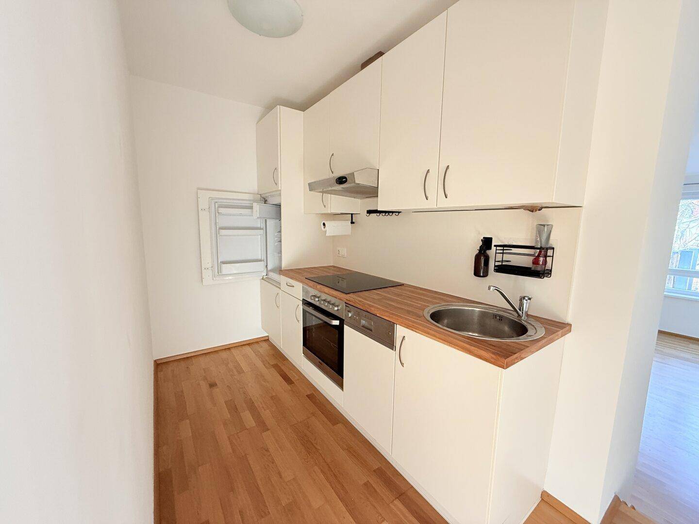 Moderne Küchenzeile mit hellen Fronten und Holz-Arbeitsplatte, praktisch und platzsparend.
