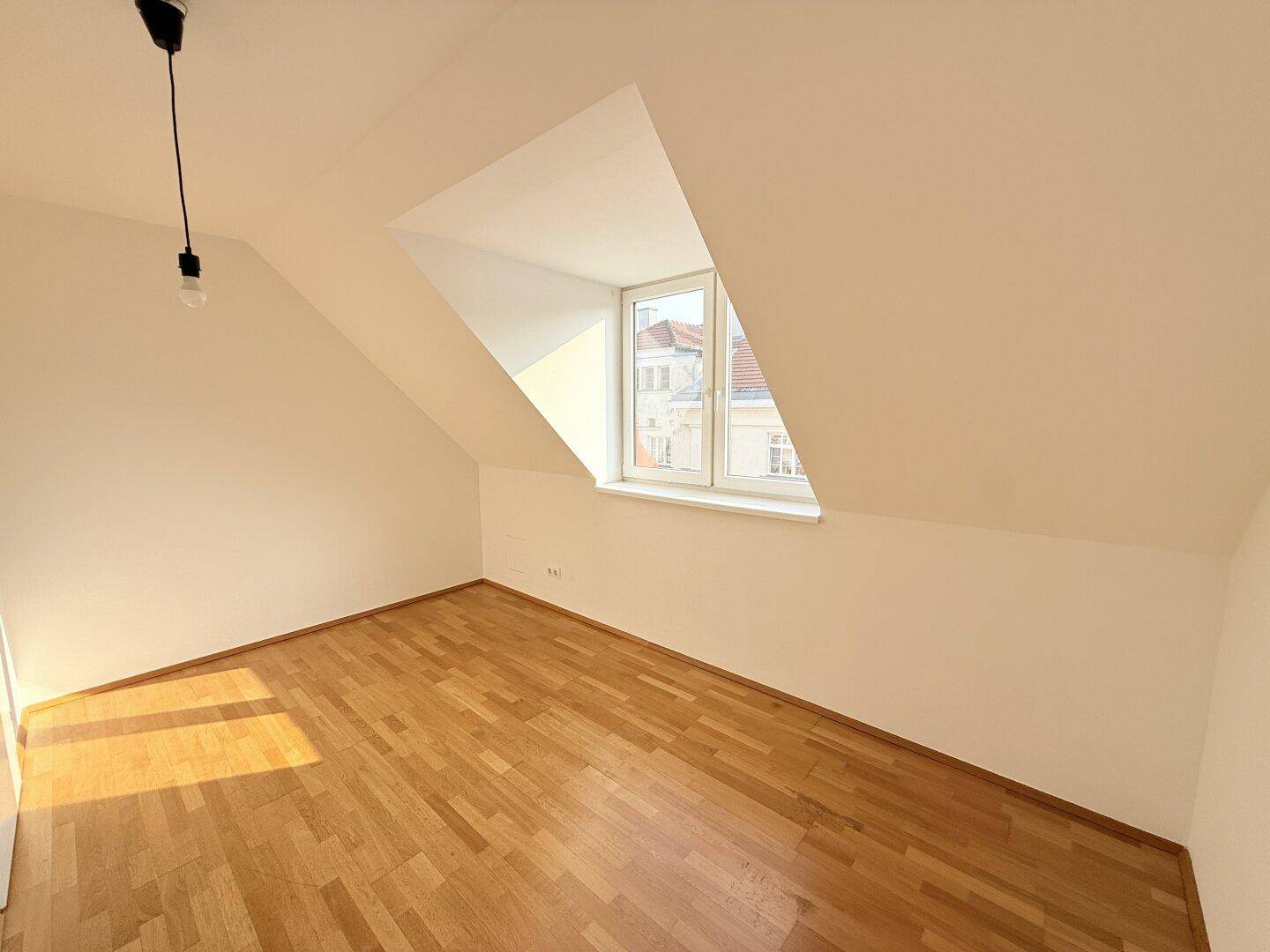 Sonniger Raum mit Parkettboden und Dachschräge, durchflutet von natürlichem Tageslicht.