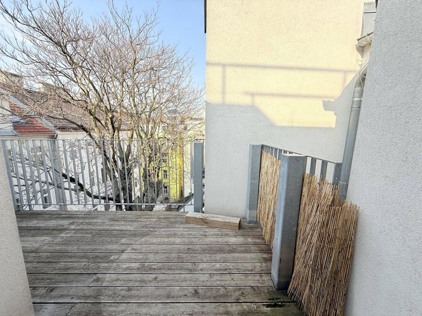 Balkon mit Holzboden und Metallgeländer, bietet einen Ausblick auf die städtische Umgebung.