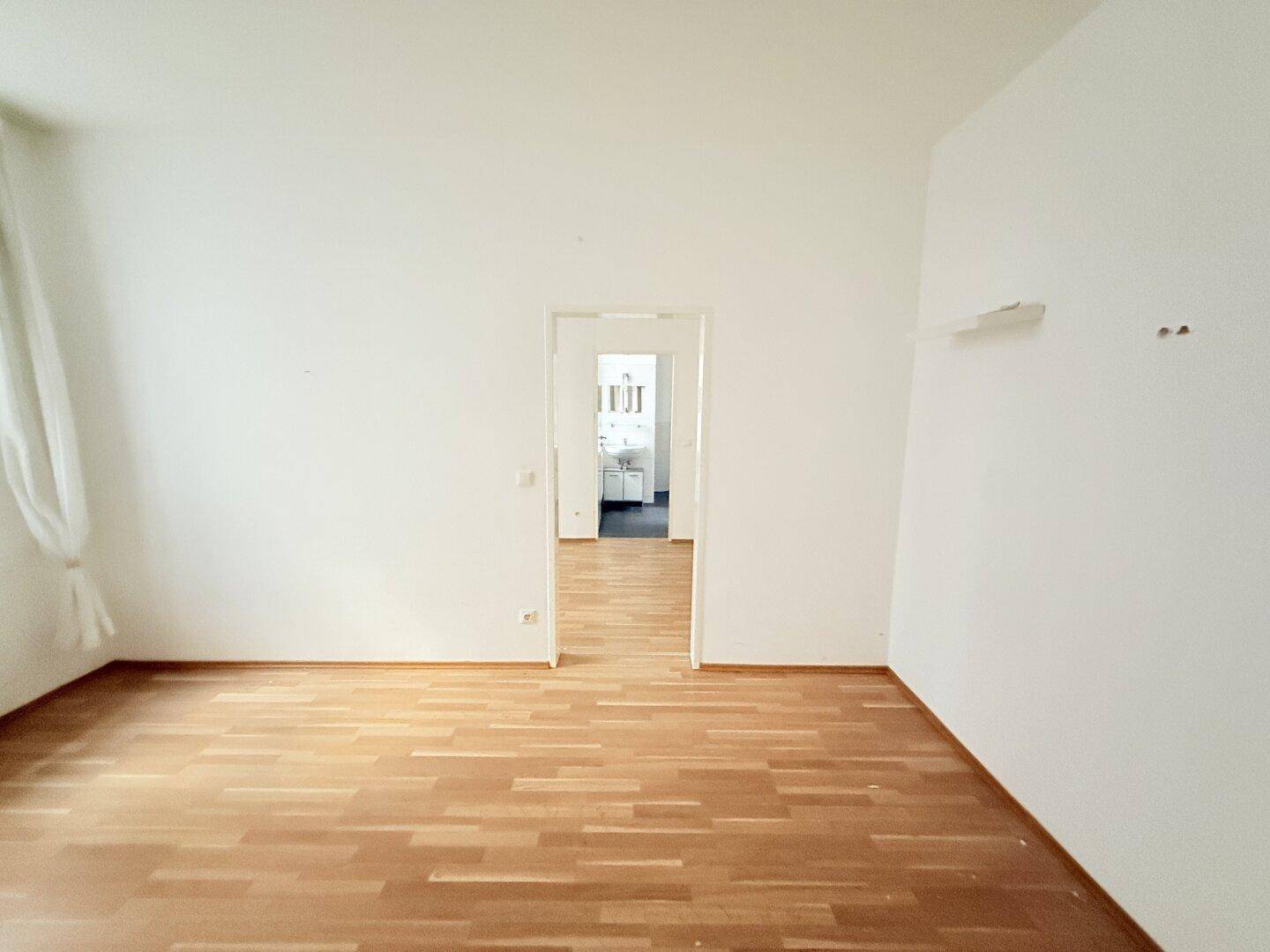 Leerer Raum mit Holzparkettboden und einem Durchgang zu einem weiteren Zimmer.