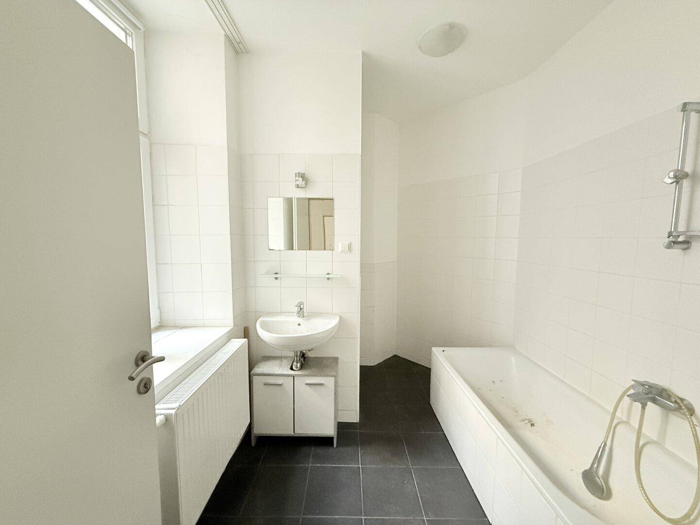 Badezimmer mit Badewanne, Waschbecken, Spiegel und einem Fenster für Tageslicht.