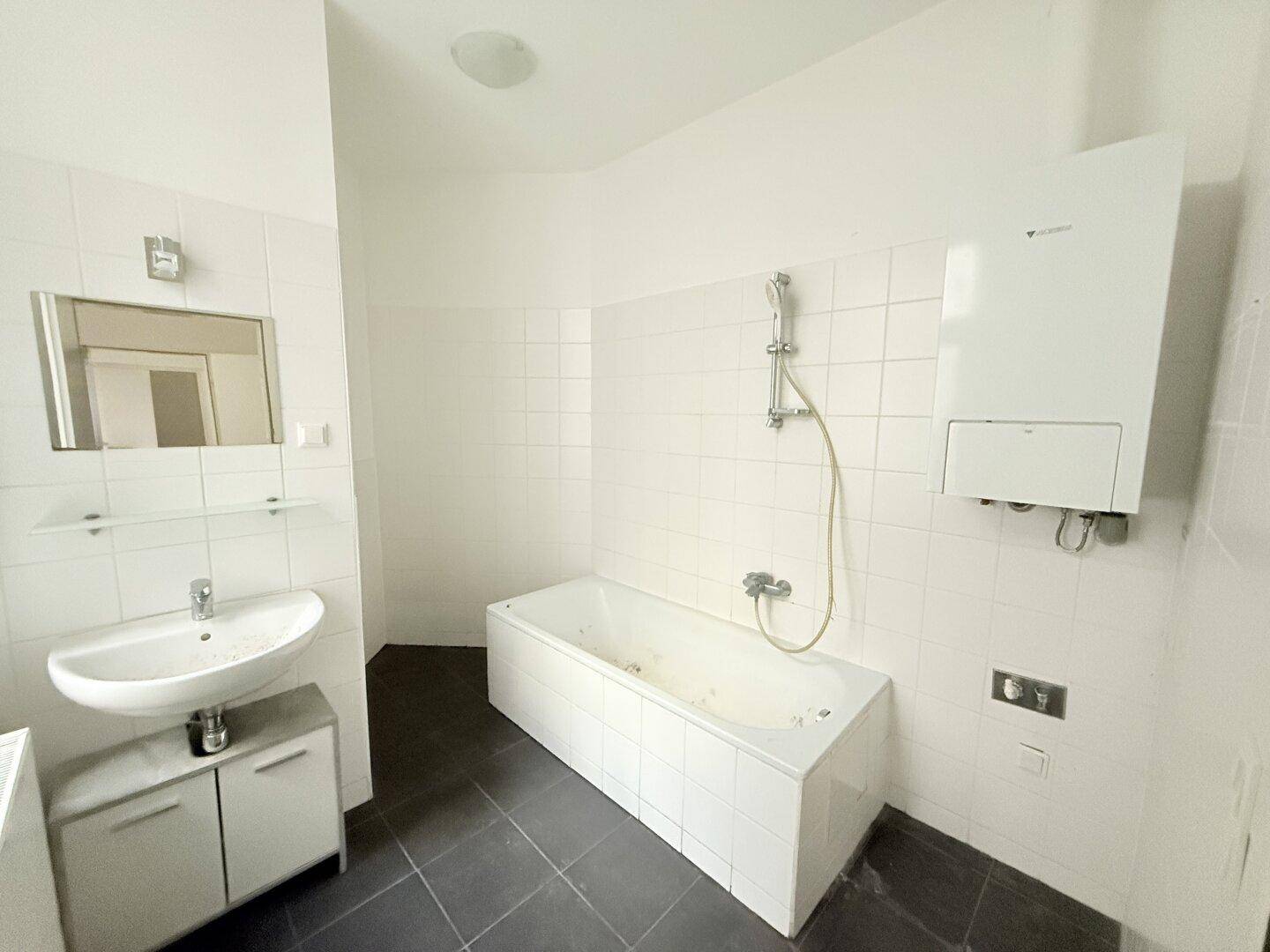 Badezimmer mit Badewanne, Waschbecken und einem an der Wand montierten Warmwasserbereiter.