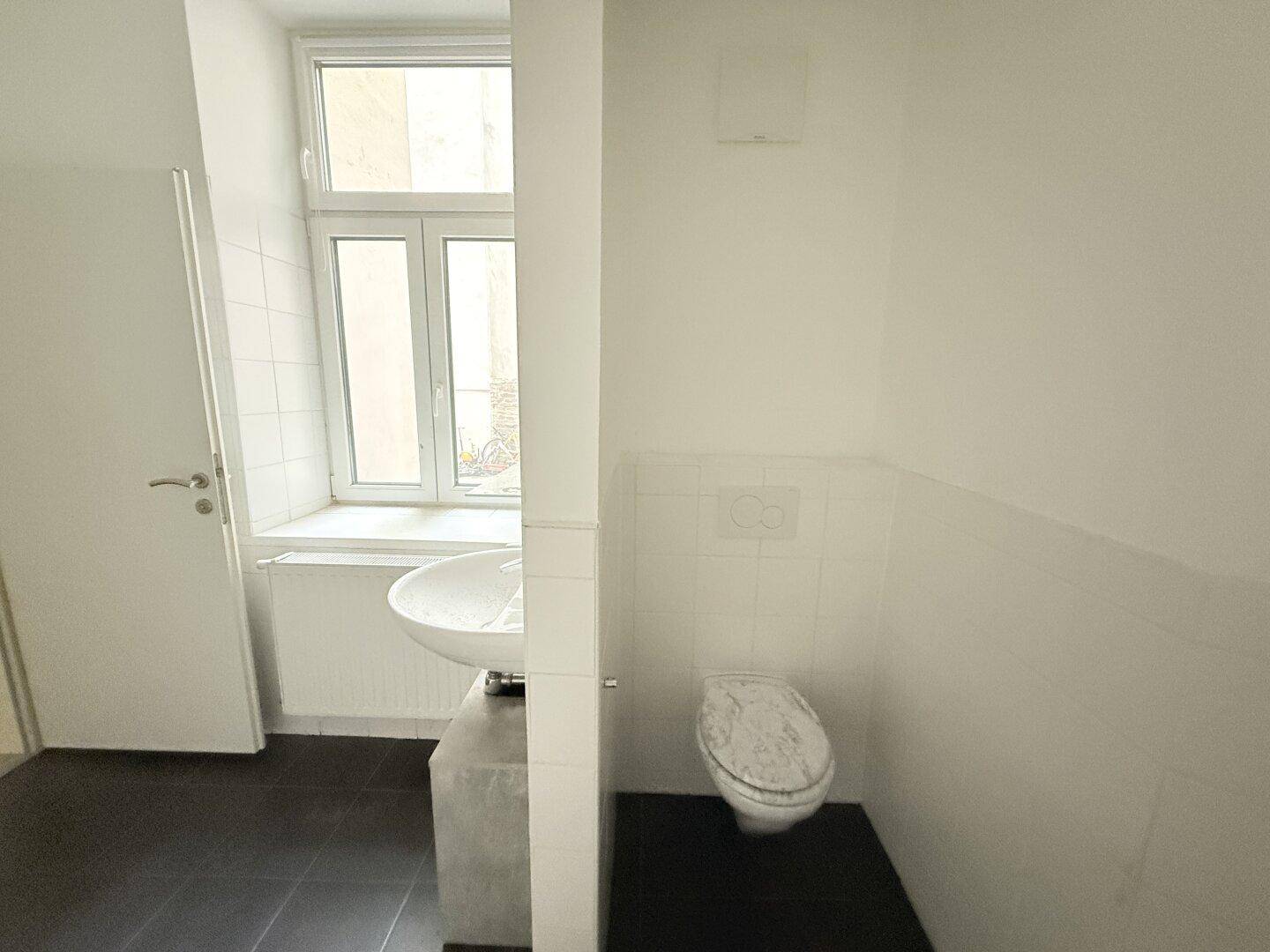 Separates WC mit Waschbecken, Toilette und einem Fenster für natürliche Belüftung.