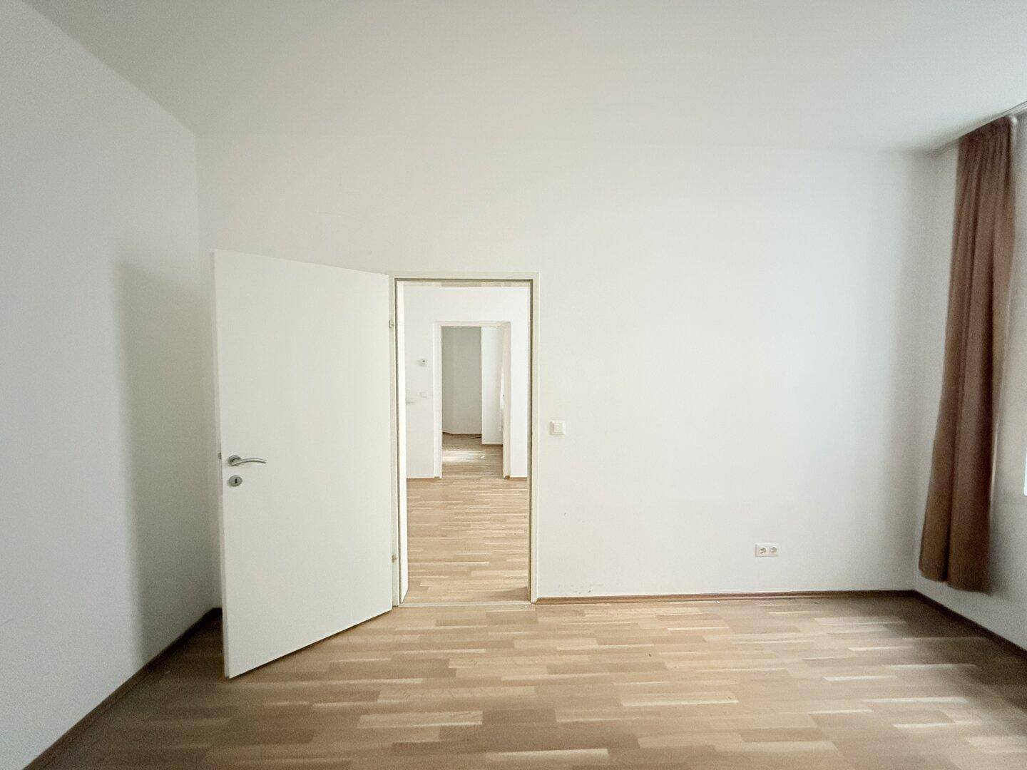 Leerer Raum mit Holzparkettboden und einer weit geöffneten Tür zu einem weiteren Bereich.