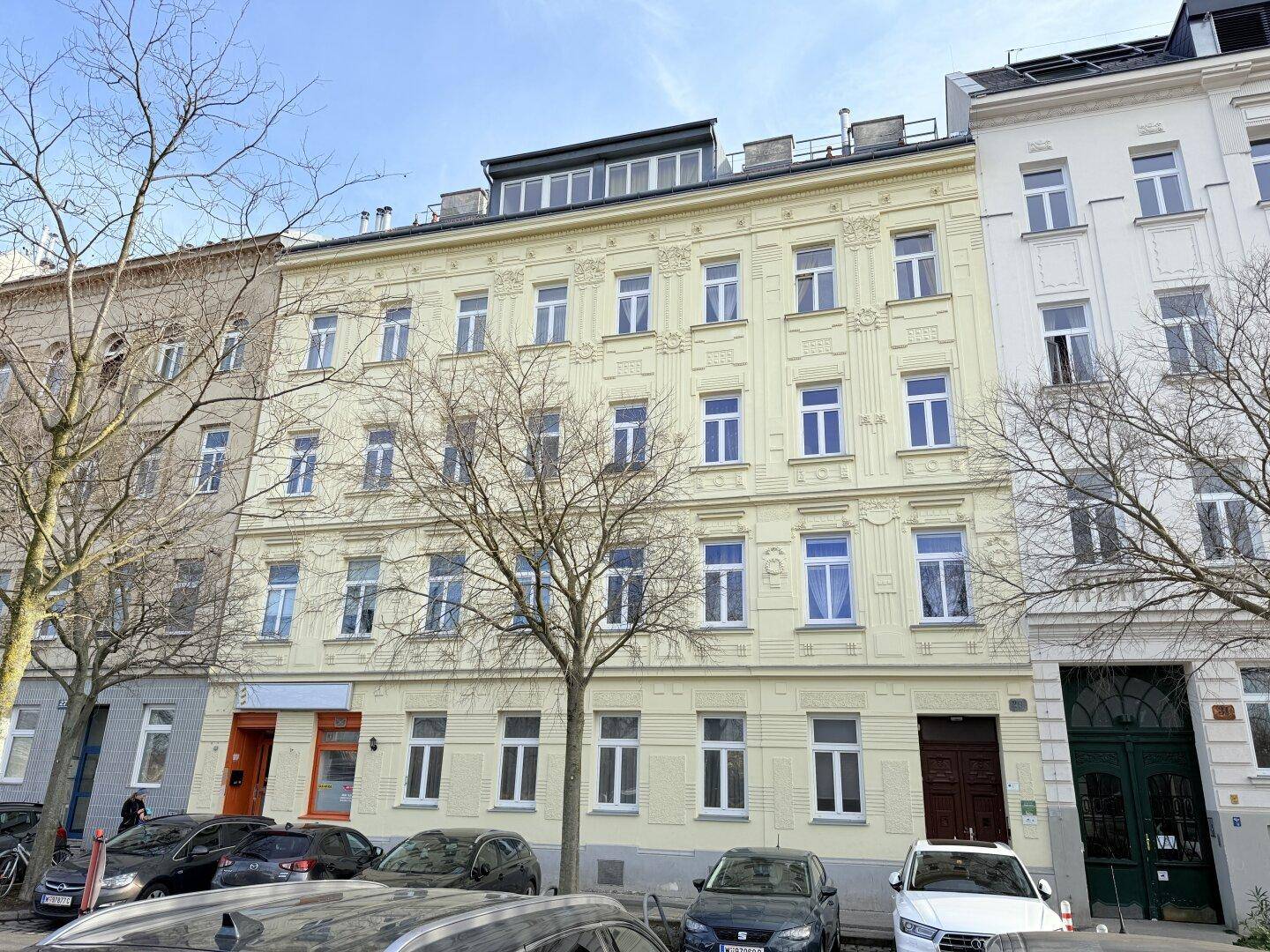 Historisches Wohngebäude mit gelber Fassade, vielen Fenstern und einem modernen Dachausbau.