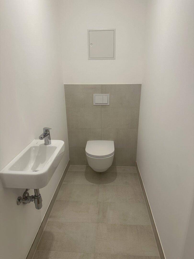 Modernes Gäste-WC mit wandhängender Toilette und kleinem Waschbecken, hell gefliest und funktional.