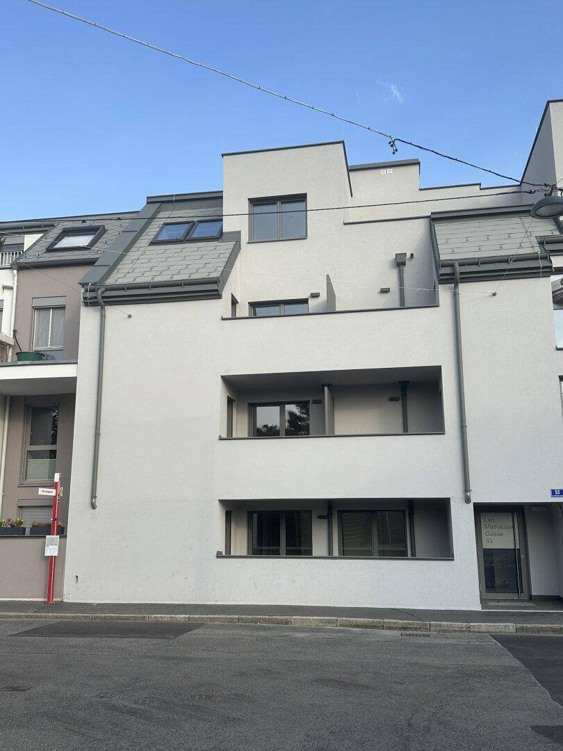 Moderne Fassade eines Mehrfamilienhauses mit klaren Linien, Balkonen und verschiedenen Dachformen.