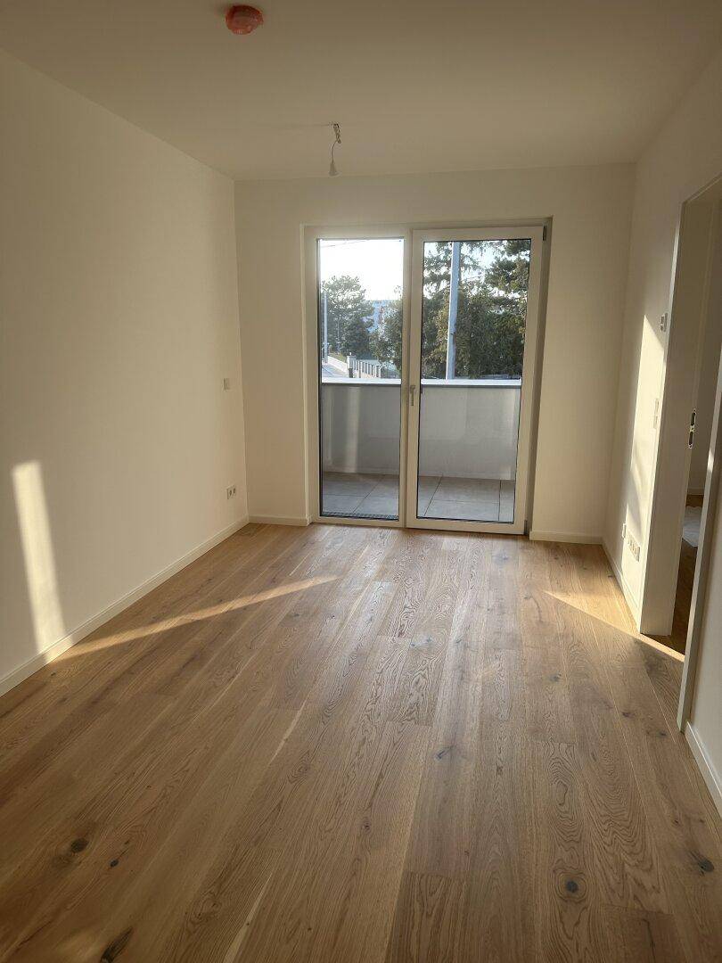 Heller Wohnraum mit Parkettboden und großem Fenster mit Zugang zu einem Balkon.
